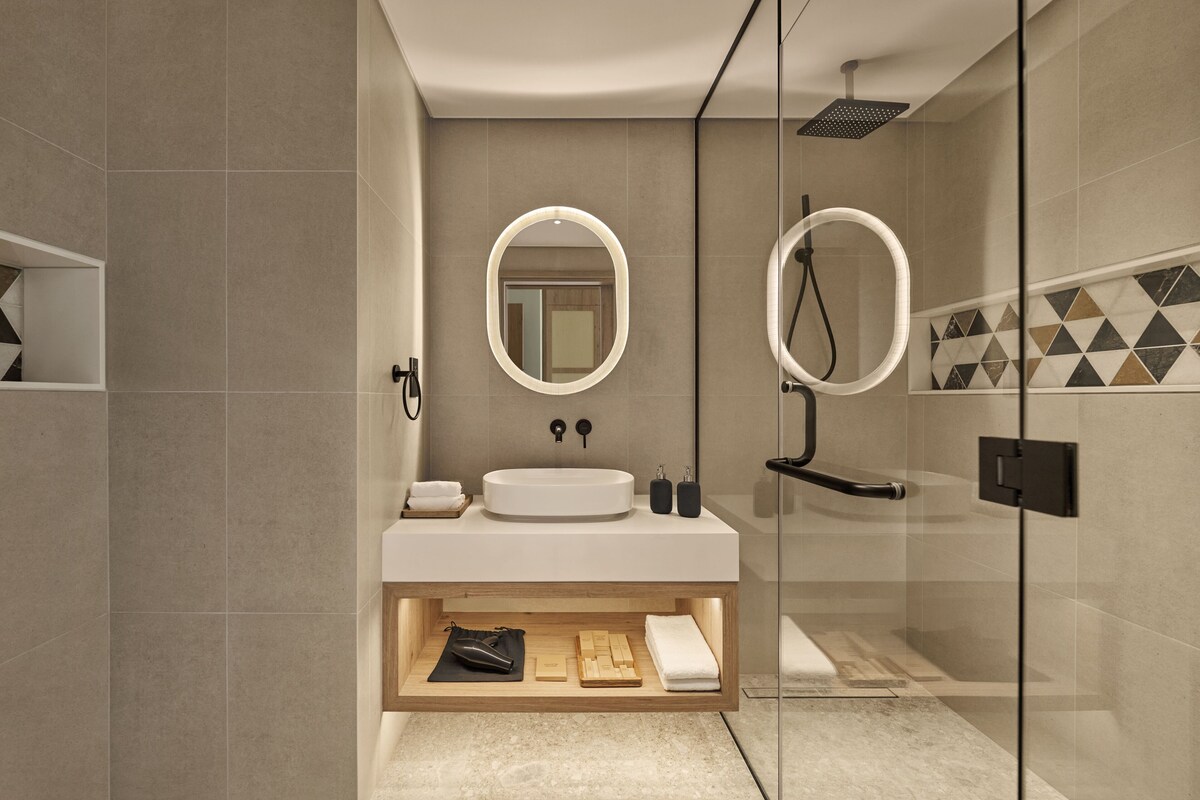 A modern bathroom with a glass shower enclosure, a vanity with a sink, and a mirror with a light.