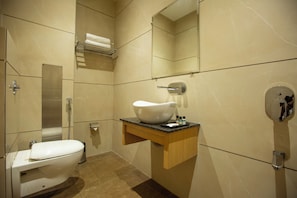 A bathroom with a toilet, sink, mirror, towel rack, and shower. - Hotel Grace (New Delhi)