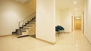 A spacious hallway with a marble floor, a staircase with metal railings, and a wooden door at the end. - Hotel Grace (New Delhi)