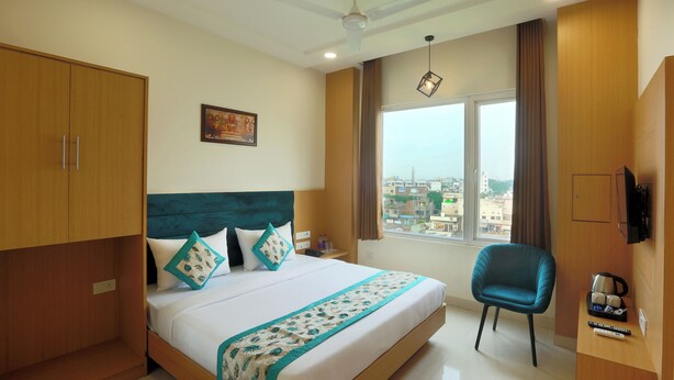 A hotel room with a large bed, a view of the city, a ceiling fan, and a TV on the wall. - Hotel Grace (New Delhi)