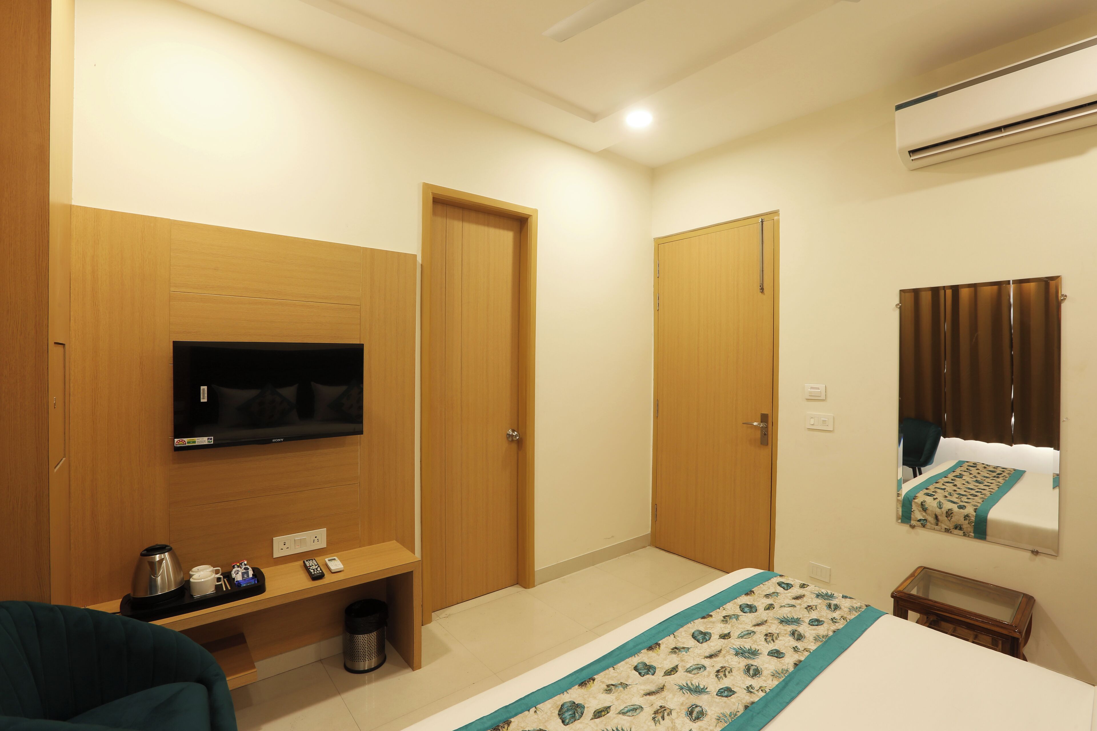 A hotel room with a bed, a TV, a small table, a chair, and a mirror.
