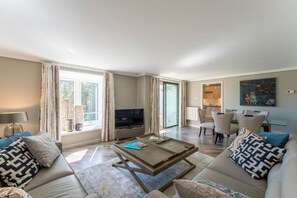 A modern living room with a sofa, coffee table, TV, and dining area. - Spacious 3BR Apartment w/ Balcony & Stunning Garden + Mountain Views! (Gleneagles Village)