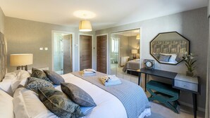 Habitación de hotel con cama, mesita de noche, lámpara, espejo y escritorio con silla.