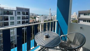 Un balcón con mesa y sillas, con vista a un paisaje urbano que incluye edificios modernos y una torre.