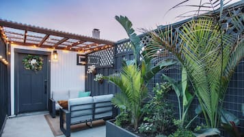 A patio with a grey bench, a decorative wreath on the door, and a garden with various plants.