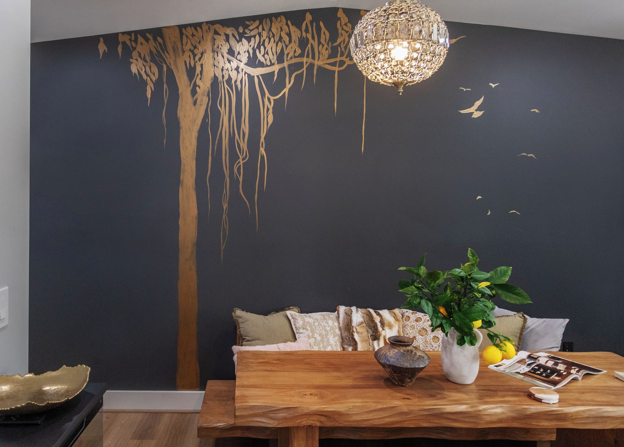 A dining area with a wooden table, a vase with a plant, and a decorative wall mural.