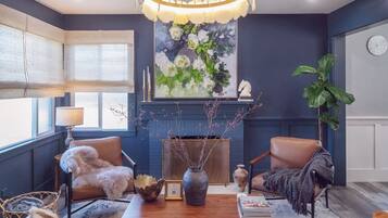 A room with a fireplace, two leather chairs, a wooden coffee table, a large painting, and a clock on the wall.