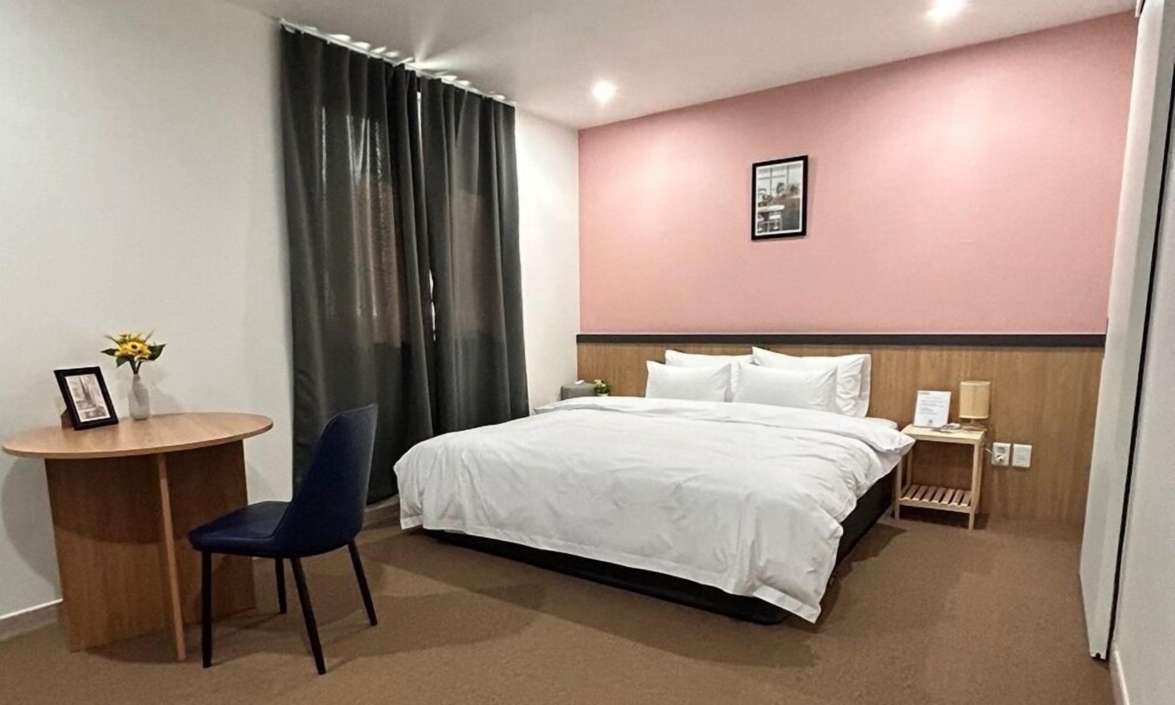 Habitación de hotel con cama, escritorio, silla, mesita de noche y un cuadro en la pared.