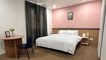 Habitación de hotel con cama, escritorio, silla, mesita de noche y un cuadro en la pared.