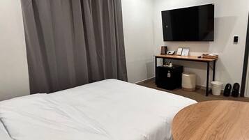 Une chambre d’hôtel comprenant un lit, un bureau avec un téléviseur à écran plat, une poubelle et un porte-chaussures.