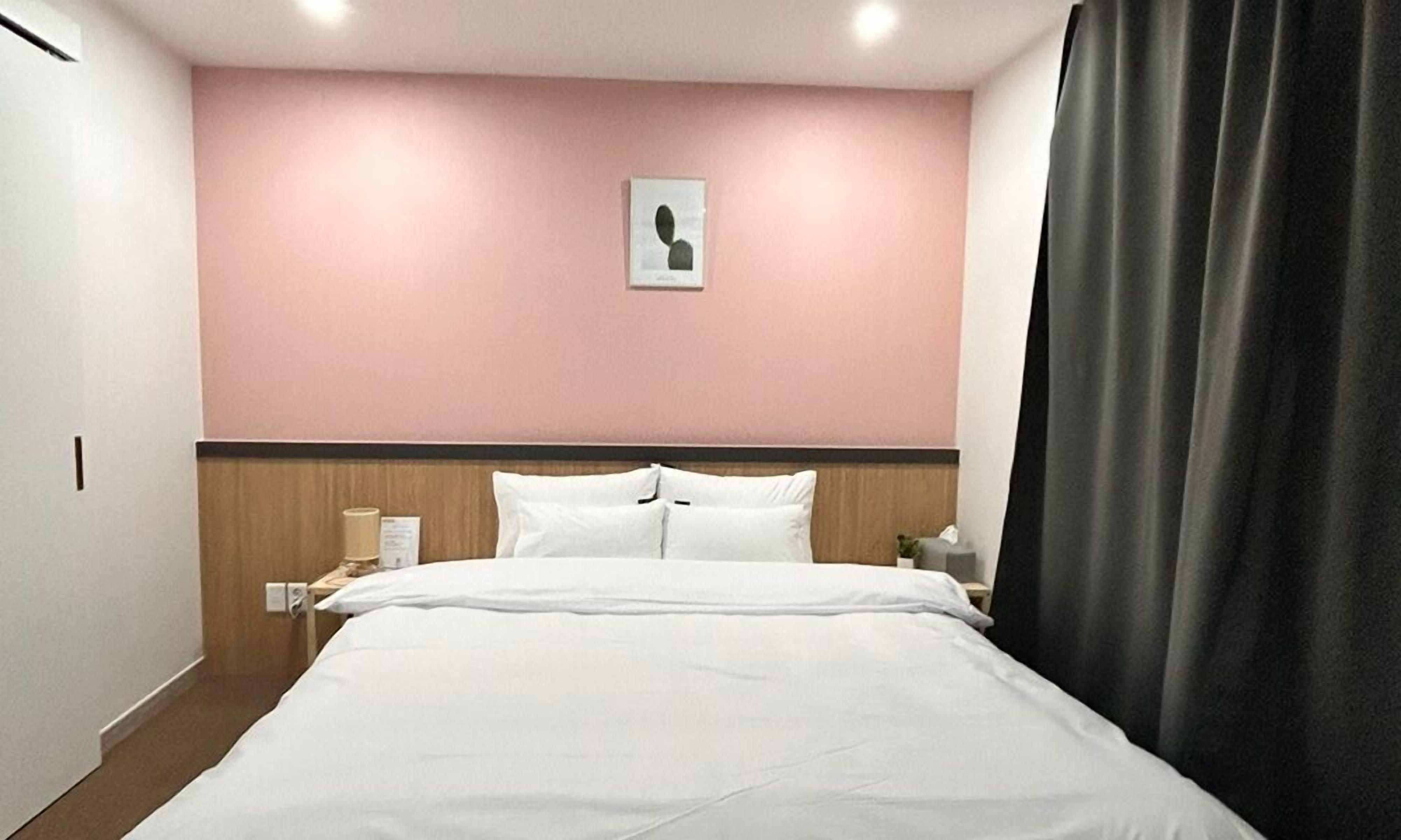 Een hotelkamer met een bed, nachtkastje, lamp, wandklok en een raam met gordijnen.