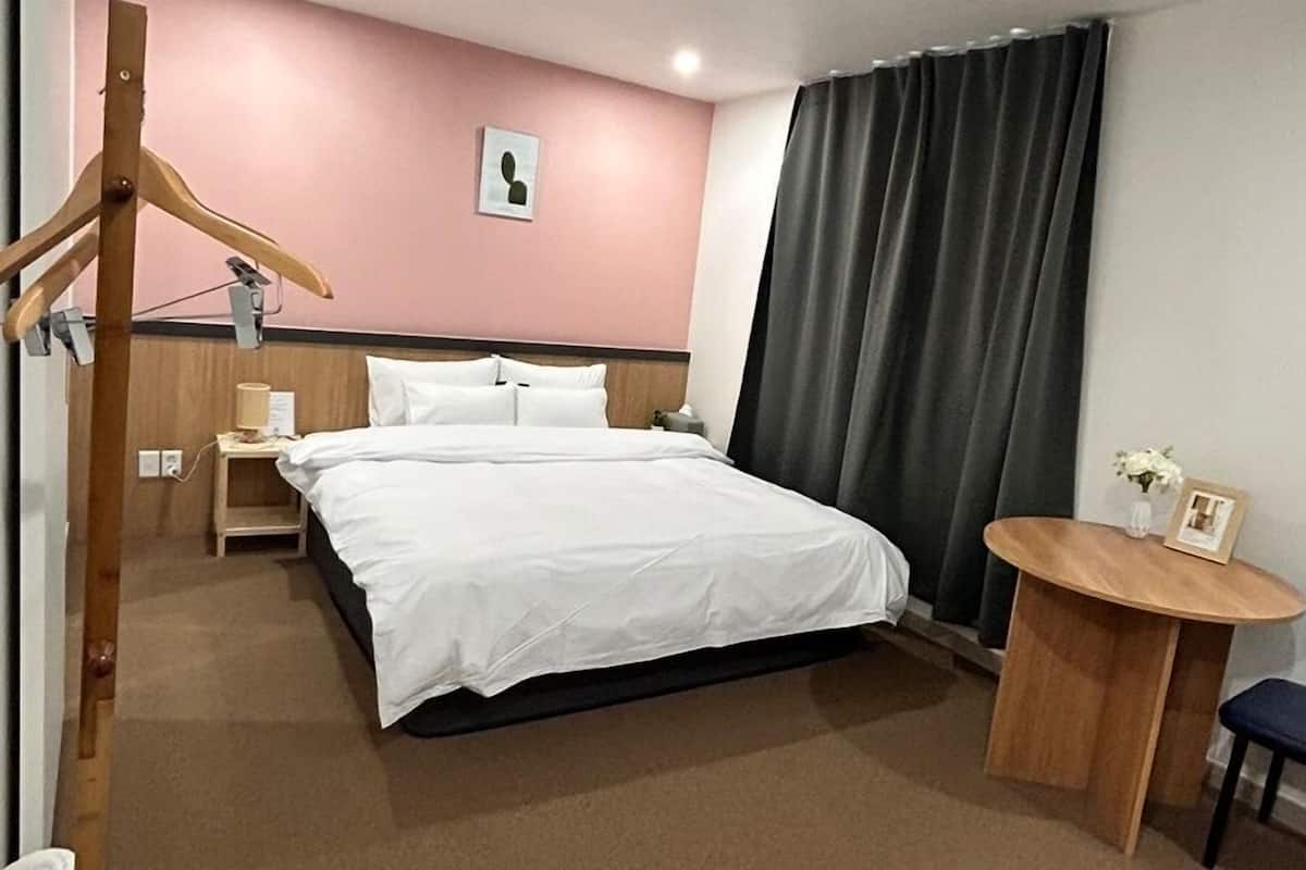 Habitación de hotel con cama, mesita de noche, lámpara y una pequeña mesa redonda con una silla.
