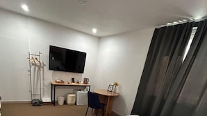 Una habitación pequeña y moderna con televisor de pantalla plana en la pared, un escritorio con silla, una mesita con un marco de fotos y un perchero.