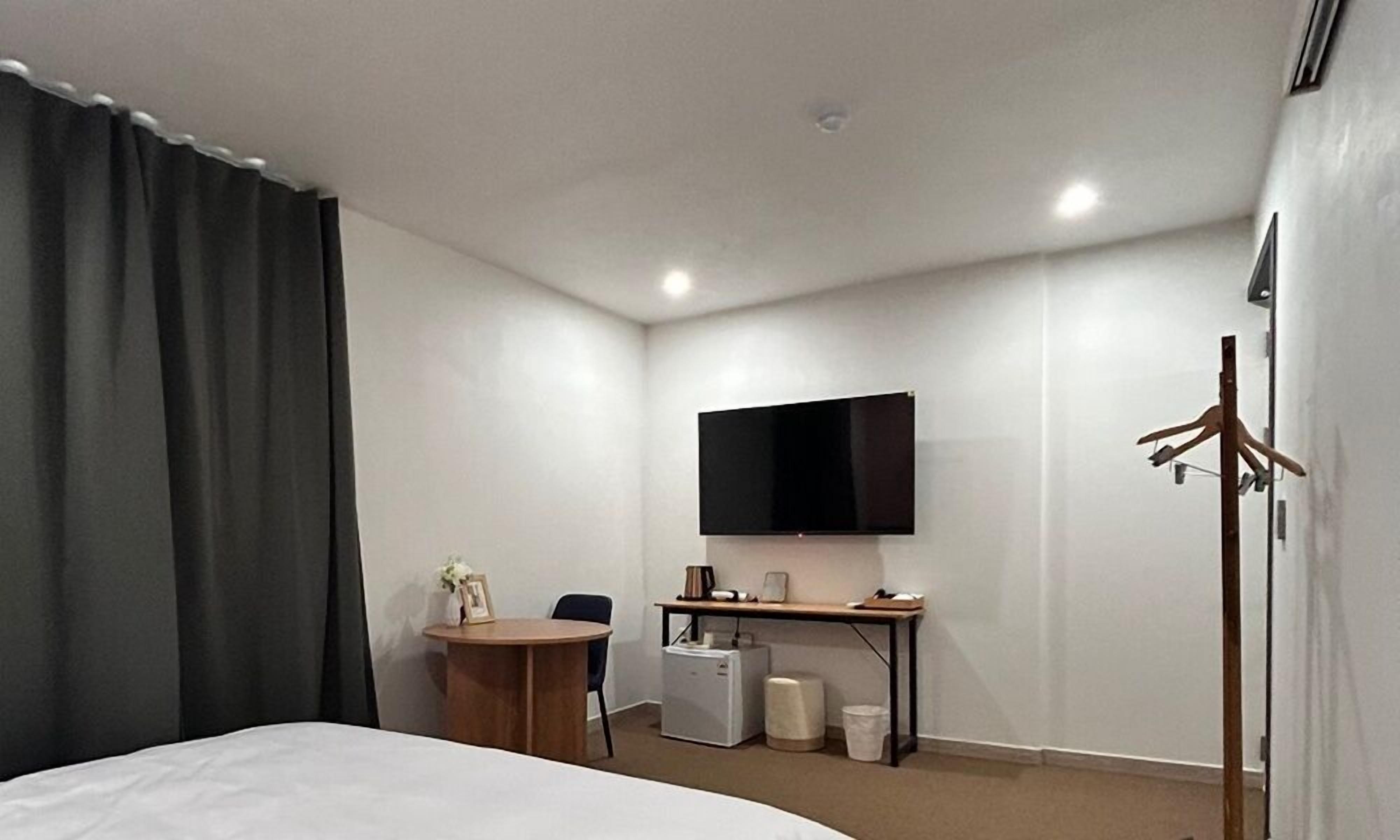 A hotel room with a bed, a desk, a TV, a small fridge, and a coat rack.