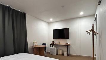 Habitación de hotel con cama, escritorio, televisor, refrigerador pequeño y perchero.
