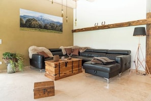 Un salon comprenant un canapé d’angle, une table basse en bois et un tableau représentant un paysage de montagne, accroché au mur.
