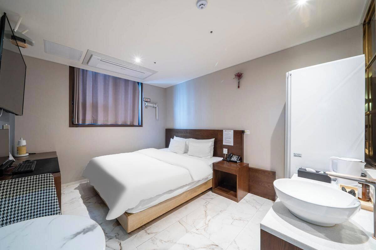 Habitación de hotel con cama, mesita de noche, televisor y baño con lavamanos y espejo.