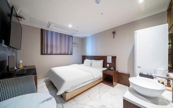 Habitación de hotel con cama, mesita de noche, televisor y baño con lavamanos y espejo.