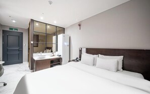 Habitación de hotel con cama, mesita de noche, espejo, lavamanos blanco y puerta.