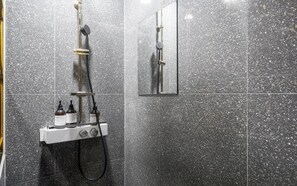 Ducha con cabezal de ducha de mano, panel de control en la pared y un espejo.