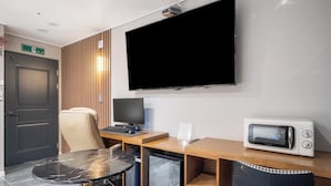 A hotel room with a flat-screen TV, a small refrigerator, a microwave, a wooden desk, a chair, and a glass table. - Brown Dot Hotel Pyeongtaek Godeok (Pyeongtaek)