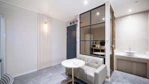 A modern hotel room with a marble-topped table, a sofa, a large mirror, and a bathroom with a sink and countertop. - Brown Dot Hotel Pyeongtaek Godeok (Pyeongtaek)