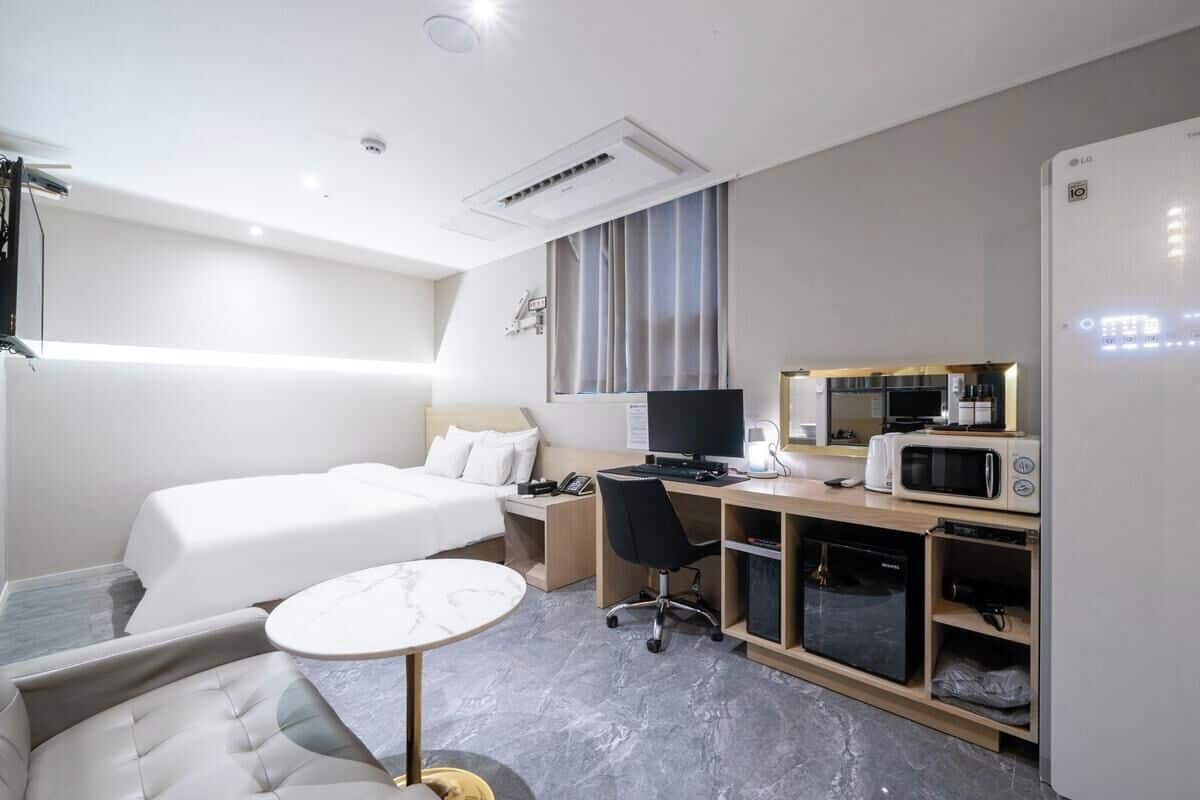 Habitación de hotel con cama, escritorio, computadora, microondas y refrigerador.