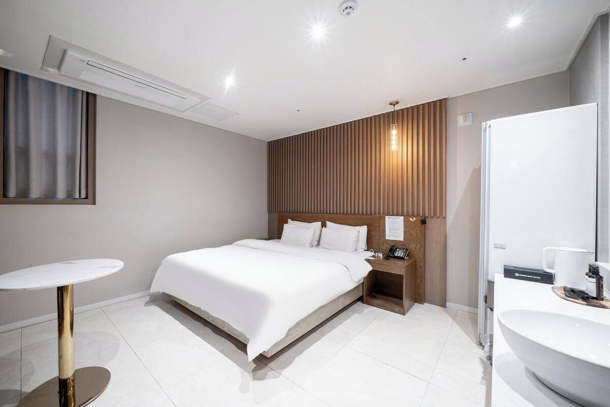 Una habitación de hotel moderna con cama, mesita de noche y baño con lavamanos y espejo.