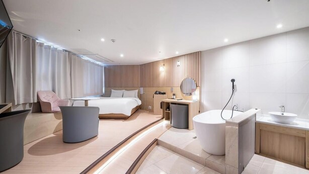 A modern hotel room with a bed, bedside table, chair, and a bathroom with a bathtub and sink. - Brown Dot Hotel Pyeongtaek Godeok (Pyeongtaek)