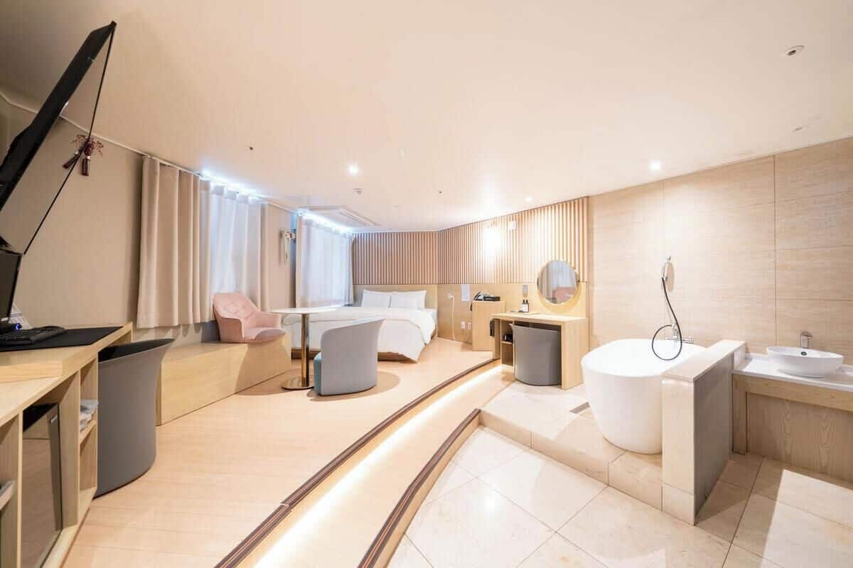 Una habitación de hotel moderna con cama, zona de estar, bañera, tocador y escritorio con lámpara.