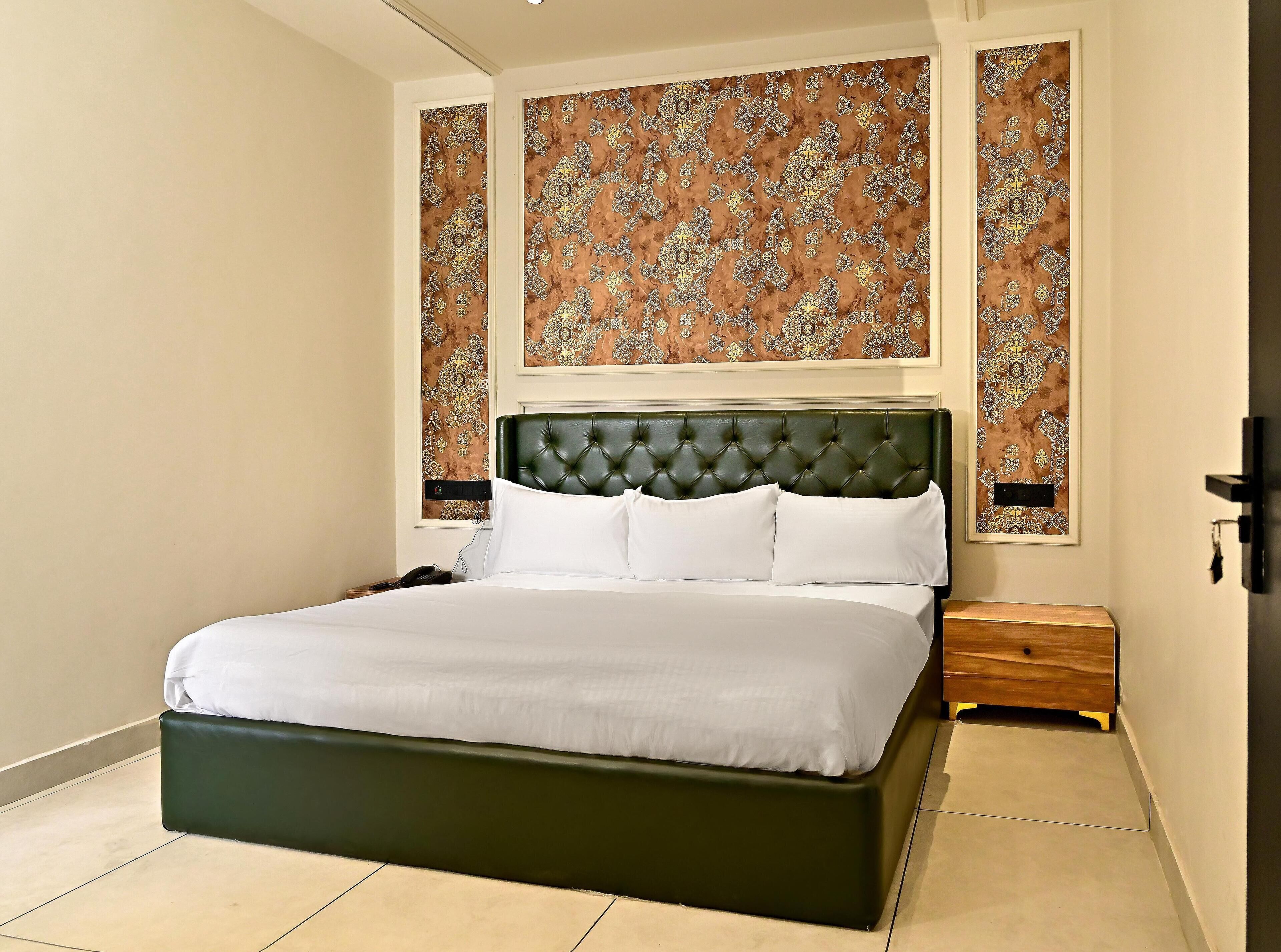 A neatly made bed with a green upholstered headboard, a bedside table, and two patterned wall decorations.