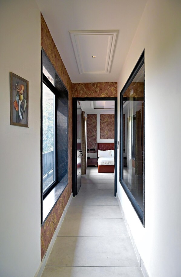 Un couloir menant à une chambre à coucher, où se trouvent un lit, un tableau accroché au mur et une fenêtre.