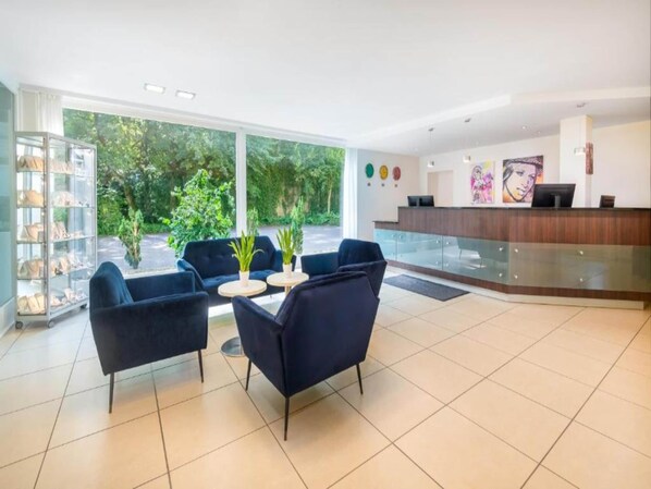 A modern hotel lobby with a reception desk, seating area, and large windows overlooking greenery. - Sunday Bielefeld Standard Double Room (Bielefeld)