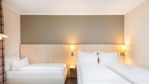 Ein Hotelzimmer mit zwei Betten, einem Holzkopfende und Wandlampen.