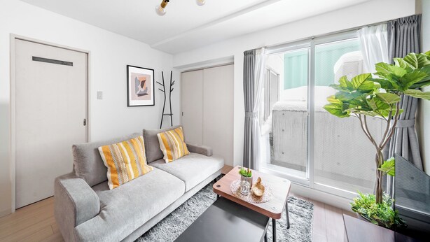 Ein modernes Wohnzimmer mit einem grauen Sofa, einem Couchtisch, einer Topfpflanze und einem großen Fenster mit Vorhängen.