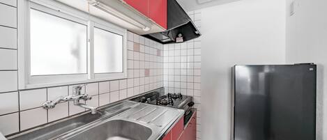 A kitchen with a stainless steel sink, red cabinets, a black refrigerator, and white tiled walls.