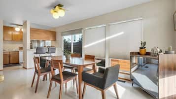 A modern kitchen with wooden cabinets, a dining area with a table and chairs, and large windows with blinds.