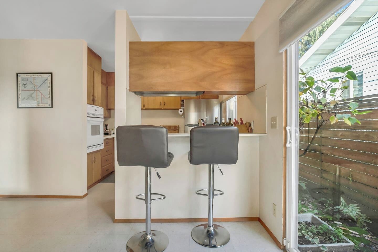 A modern kitchen with wooden cabinets, a built-in oven, and a small island with bar stools.