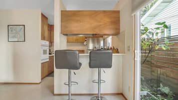 A modern kitchen with wooden cabinets, a built-in oven, and a small island with bar stools.