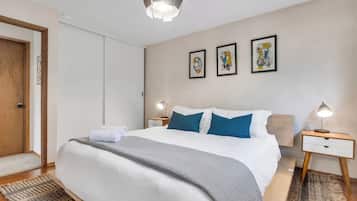 A hotel room with a bed, bedside tables, a door, and artwork on the wall.