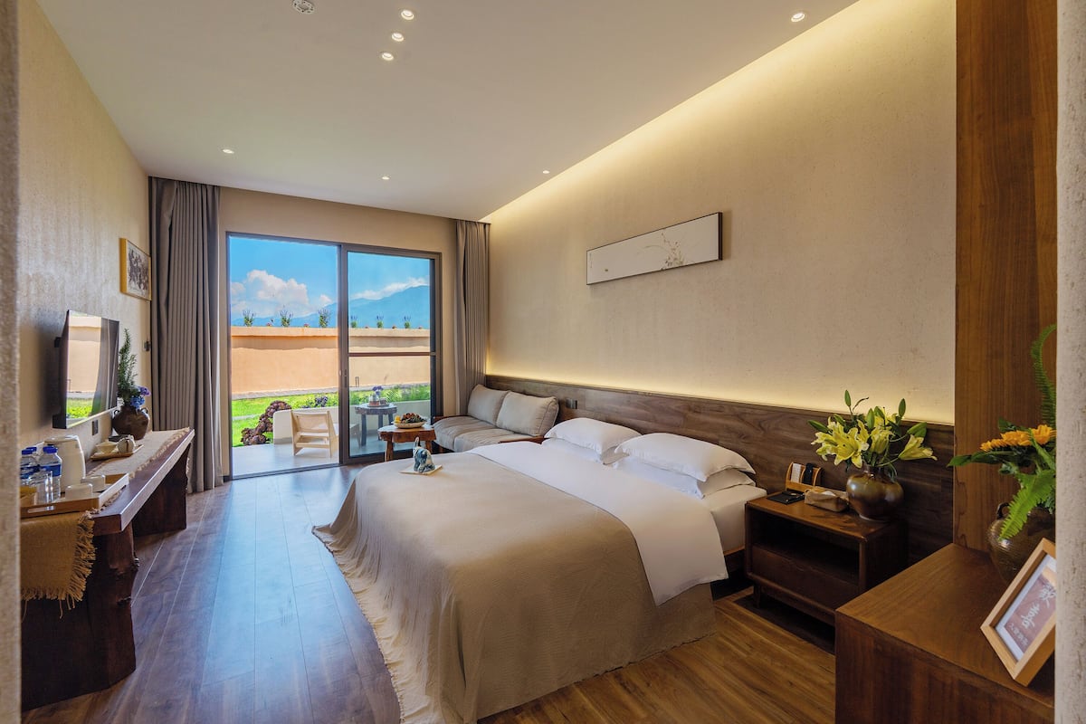 Une chambre d’hôtel avec un grand lit, un bureau, une chaise, une table de chevet et une vue sur l’extérieur.