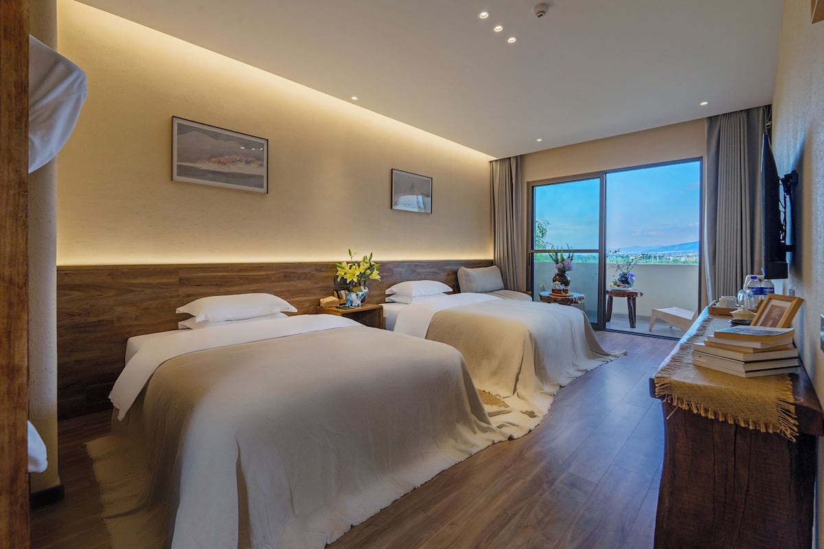Une chambre d’hôtel avec deux lits, un balcon offrant une vue agréable et un bureau avec des livres et un vase.