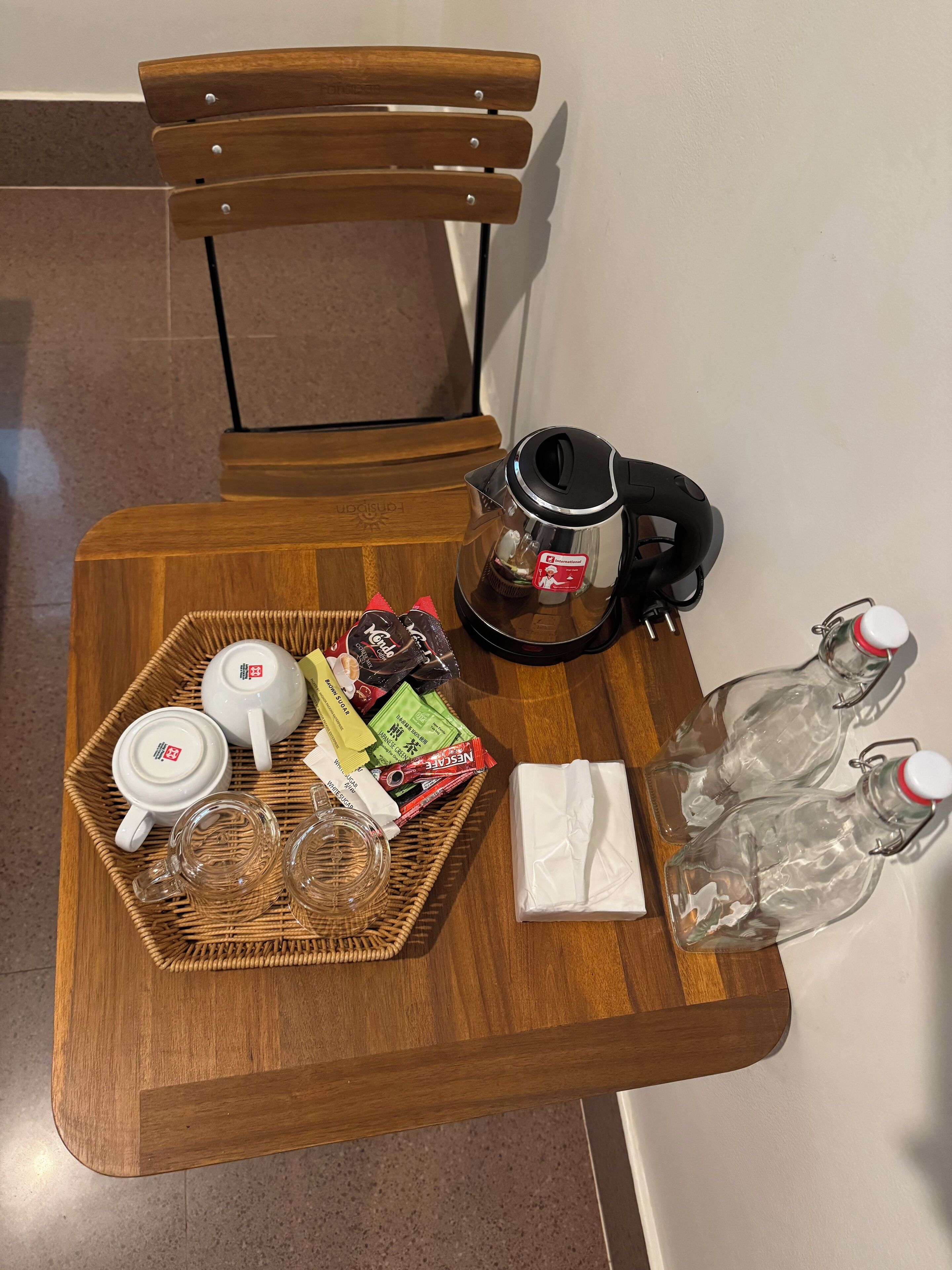 A wooden table with a tray containing a teapot, cups, and snacks, a kettle, and two water bottles.