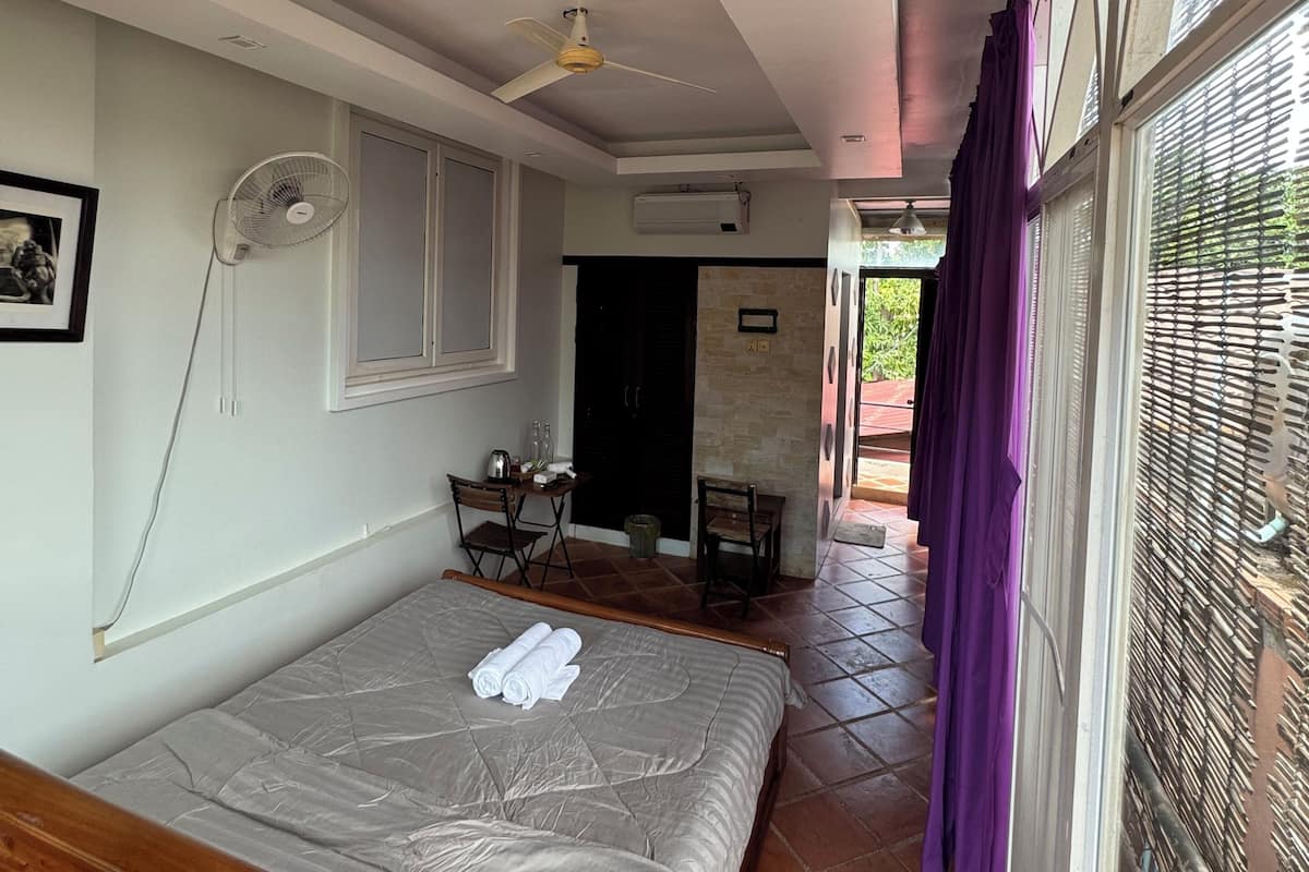 A bedroom with a bed, a ceiling fan, a window with blinds, and a view of the outside.