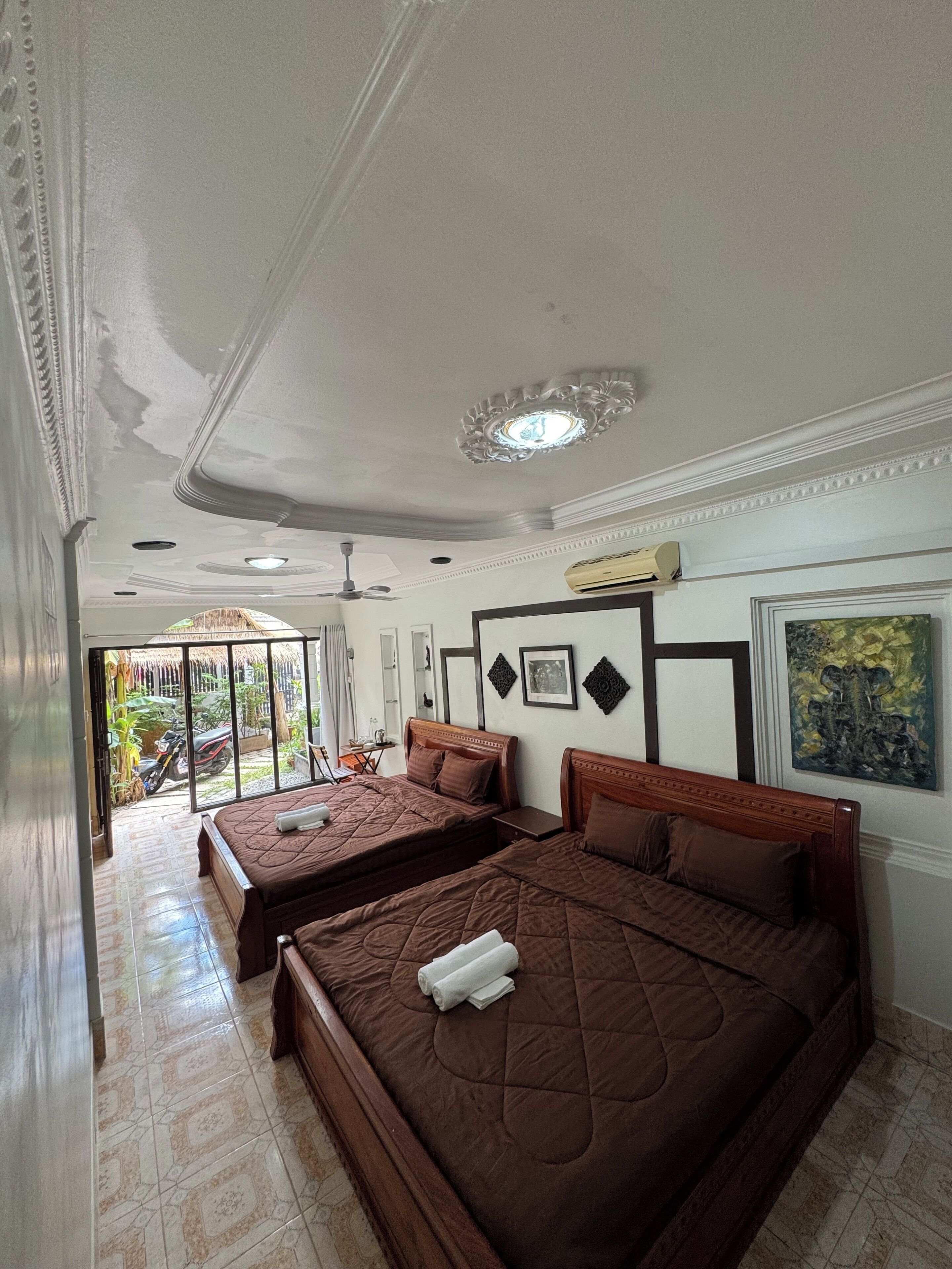 Habitación de hotel con dos camas, ventilador de techo, ventana grande y vista al exterior.