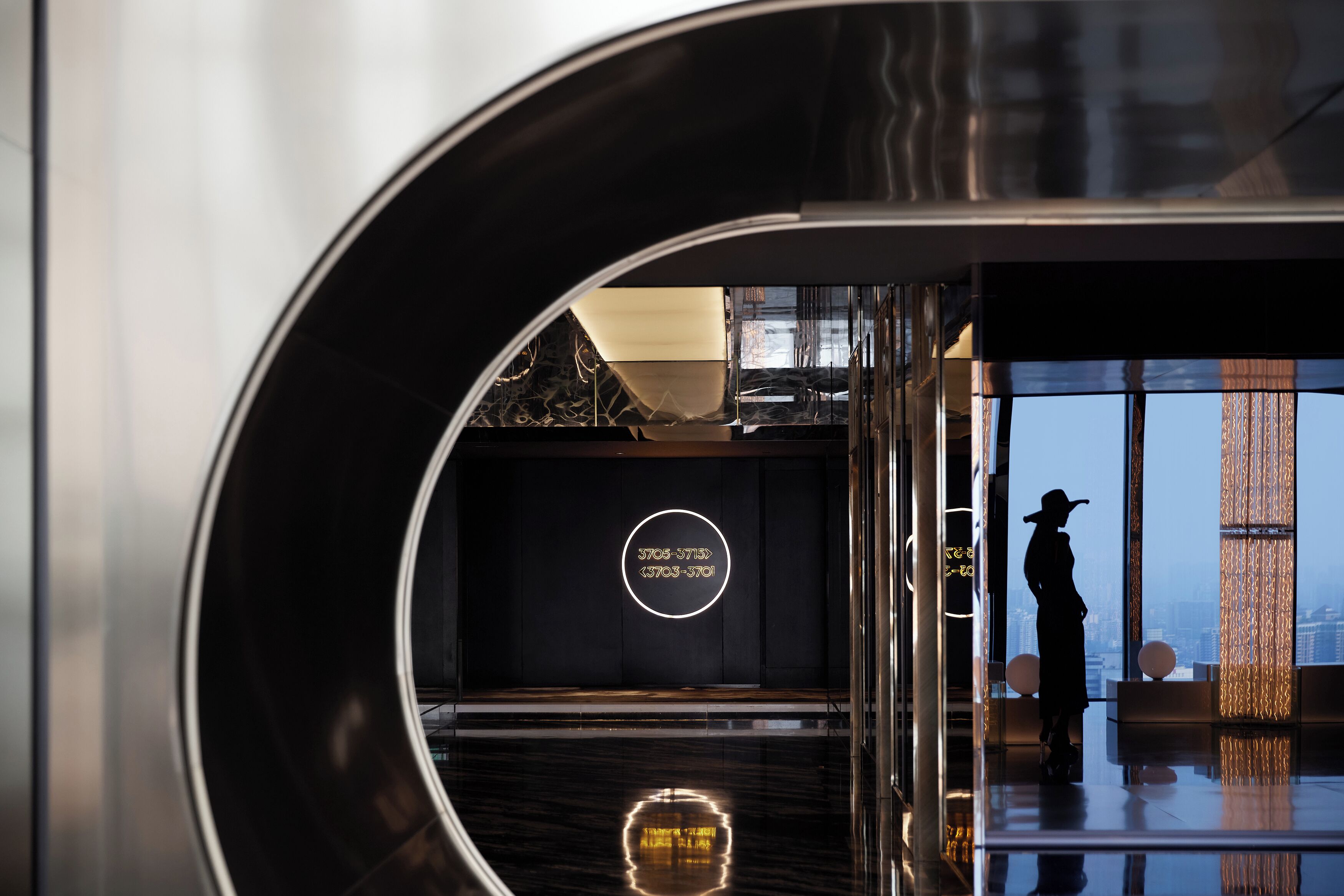 A modern interior with a reflective floor, a circular neon sign, and a silhouette of a person.