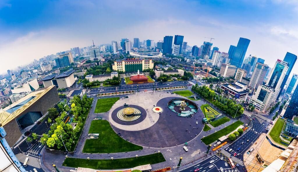 A cityscape with modern high-rise buildings, a central plaza with a circular design, and surrounding greenery.