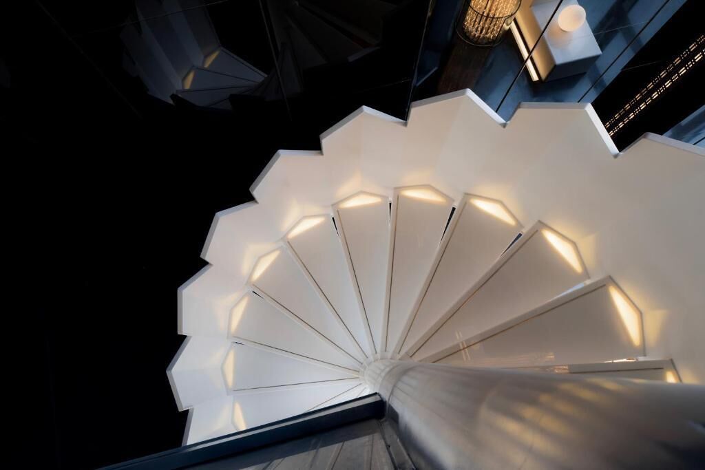 Una escalera de caracol con un diseño geométrico blanco e iluminación ambiental.