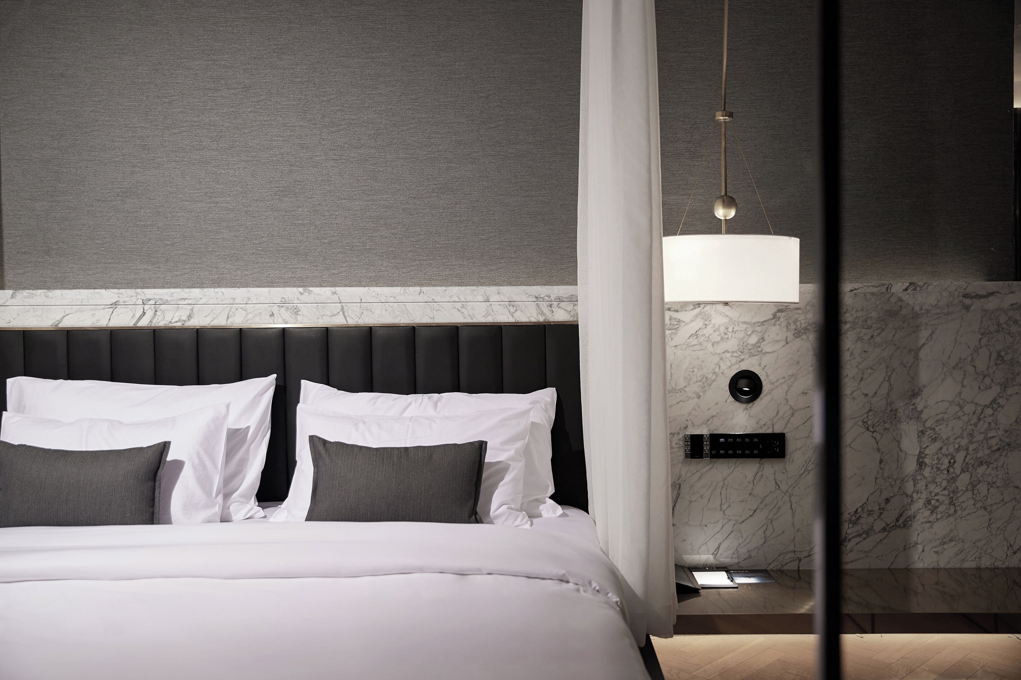 A modern hotel room with a bed, a control panel, and a marble wall.