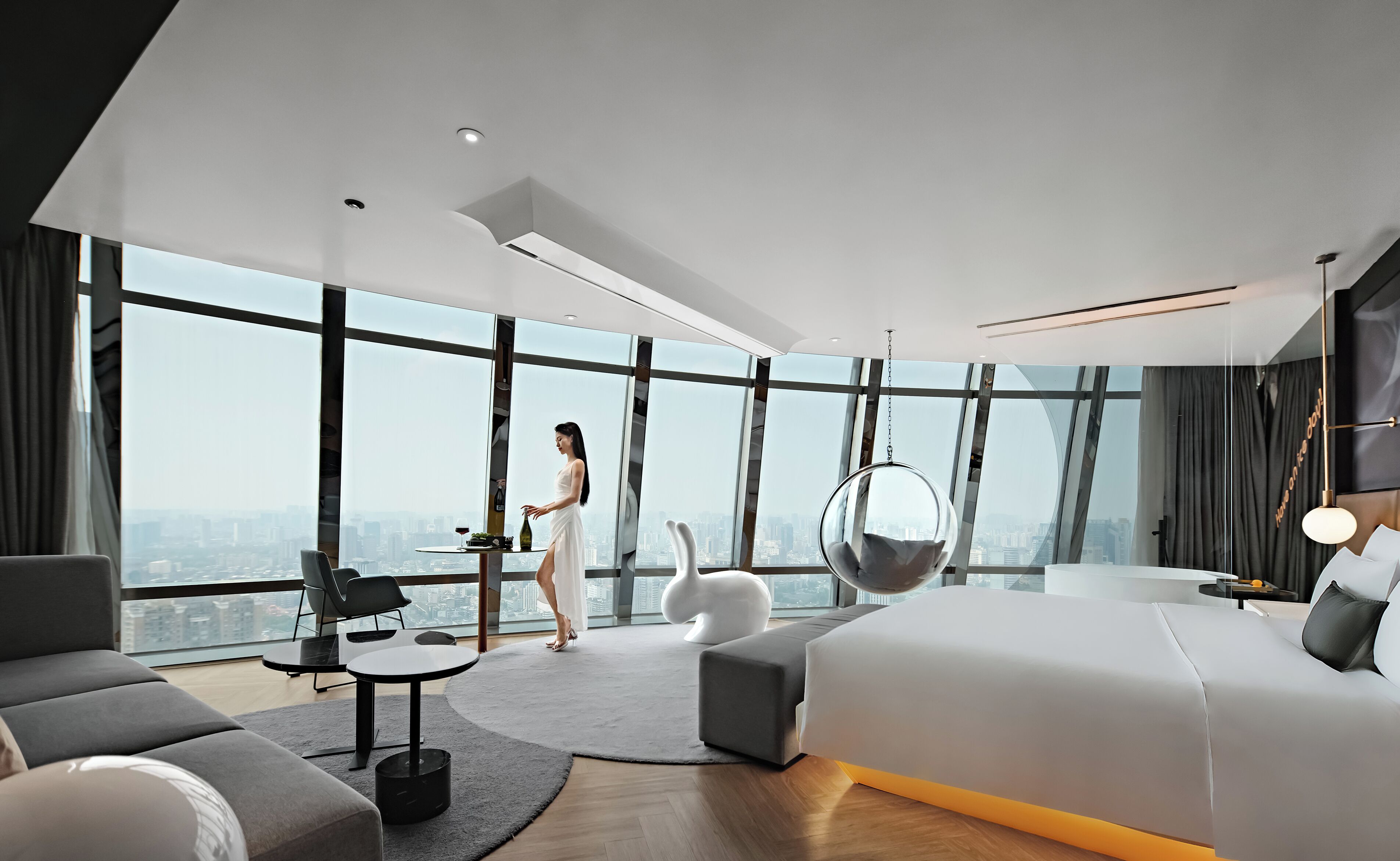 Une chambre d’hôtel moderne avec un grand lit, une table à manger, un canapé et un fauteuil suspendu.